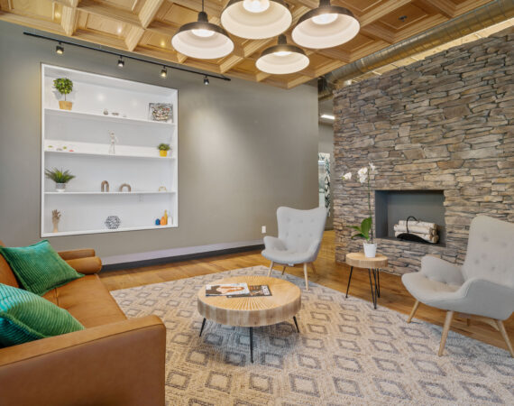 A stone accent wall with fireplace, a modern orange sofa with green pillows, and two white arm chairs